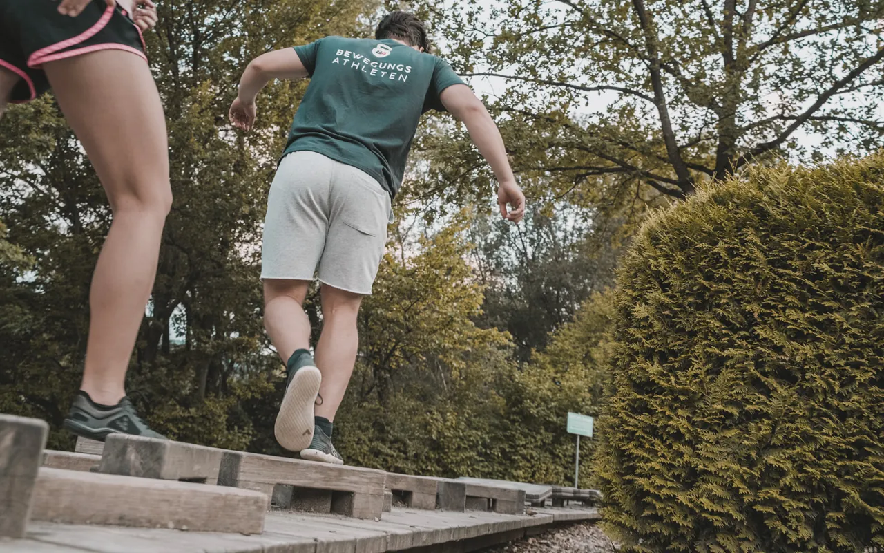 Zwei Personen balancieren in einem Park über Holzbalken