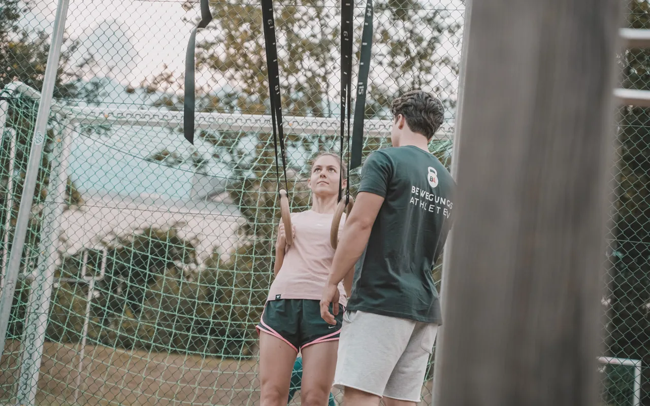 Philipp Schmitt steht neben einer Kundin am Schlingentrainer im Calisthenics-Park