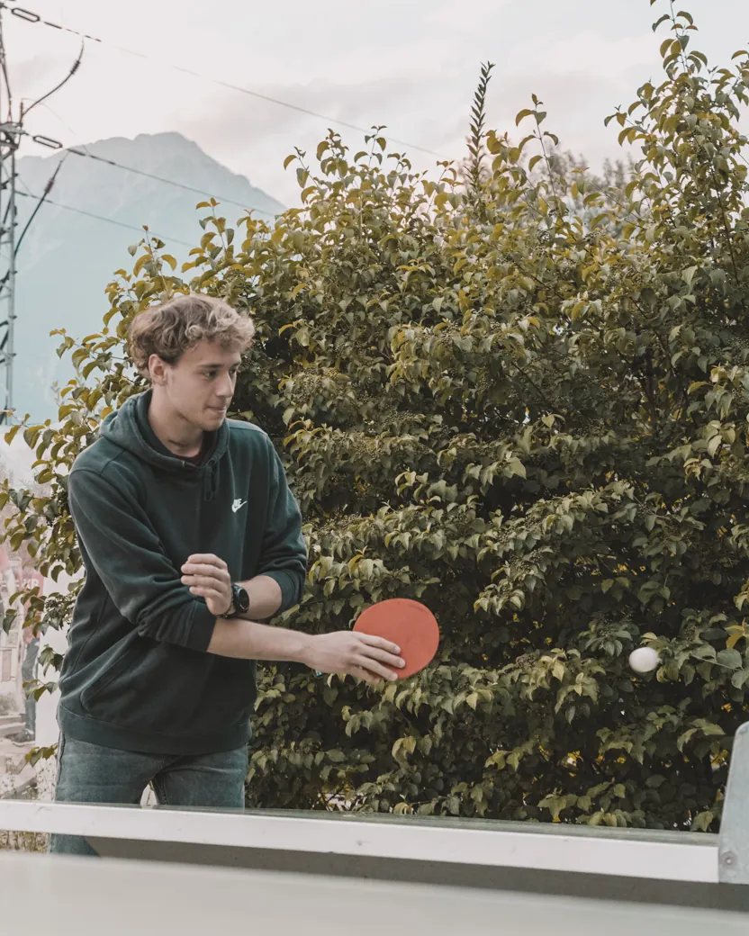 Ein junger Mann spielt im Freien Tischtennis, im Hintergrund Berge