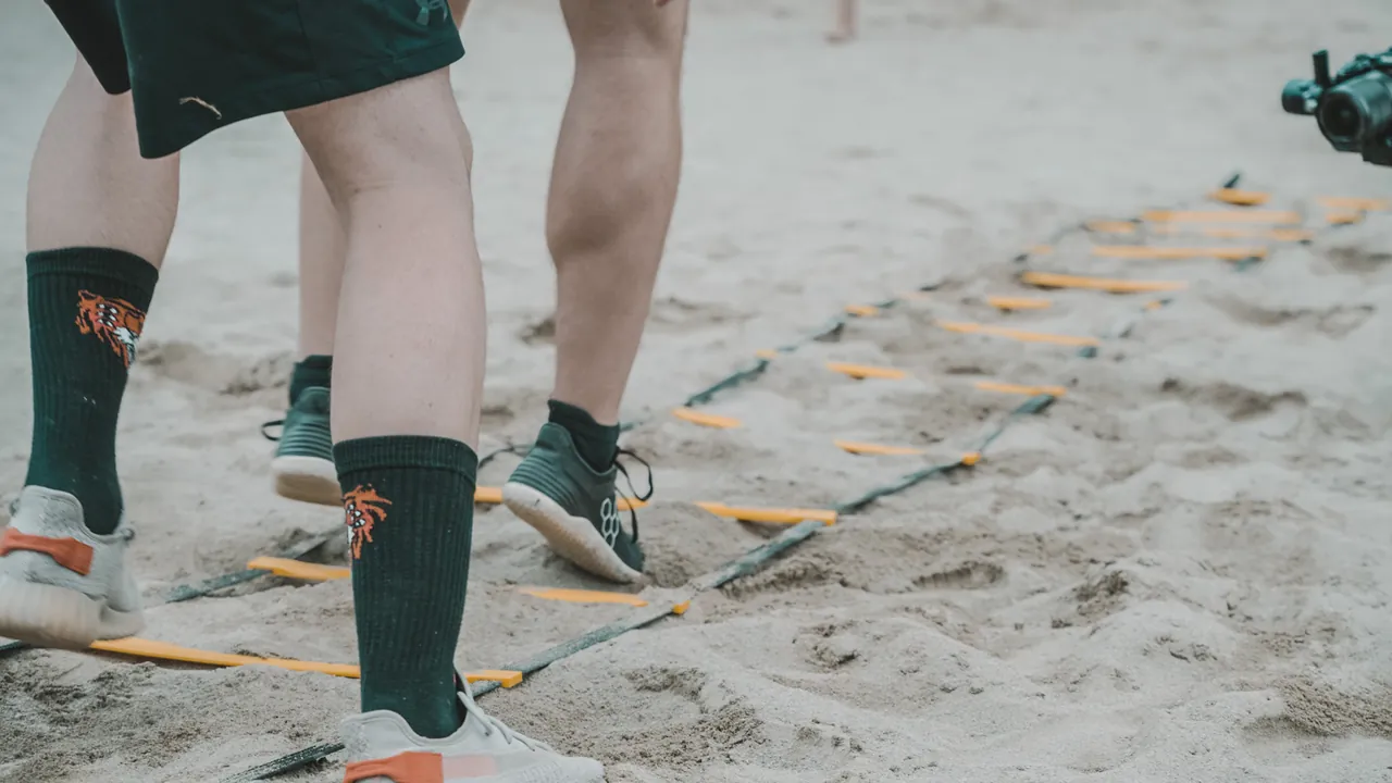 Zwei Personen laufen im Sand durch eine Koordinationsleiter