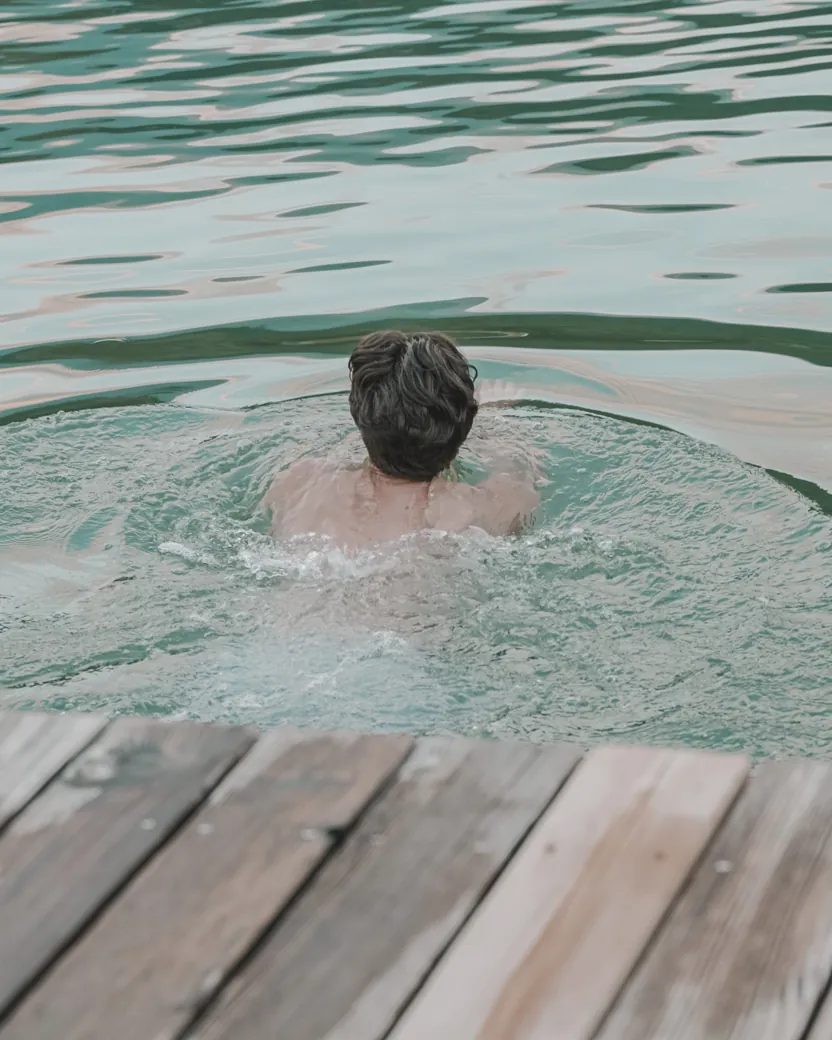 Ein junger Mann schwimmt von einem Holzsteg aus in einen Bergsee